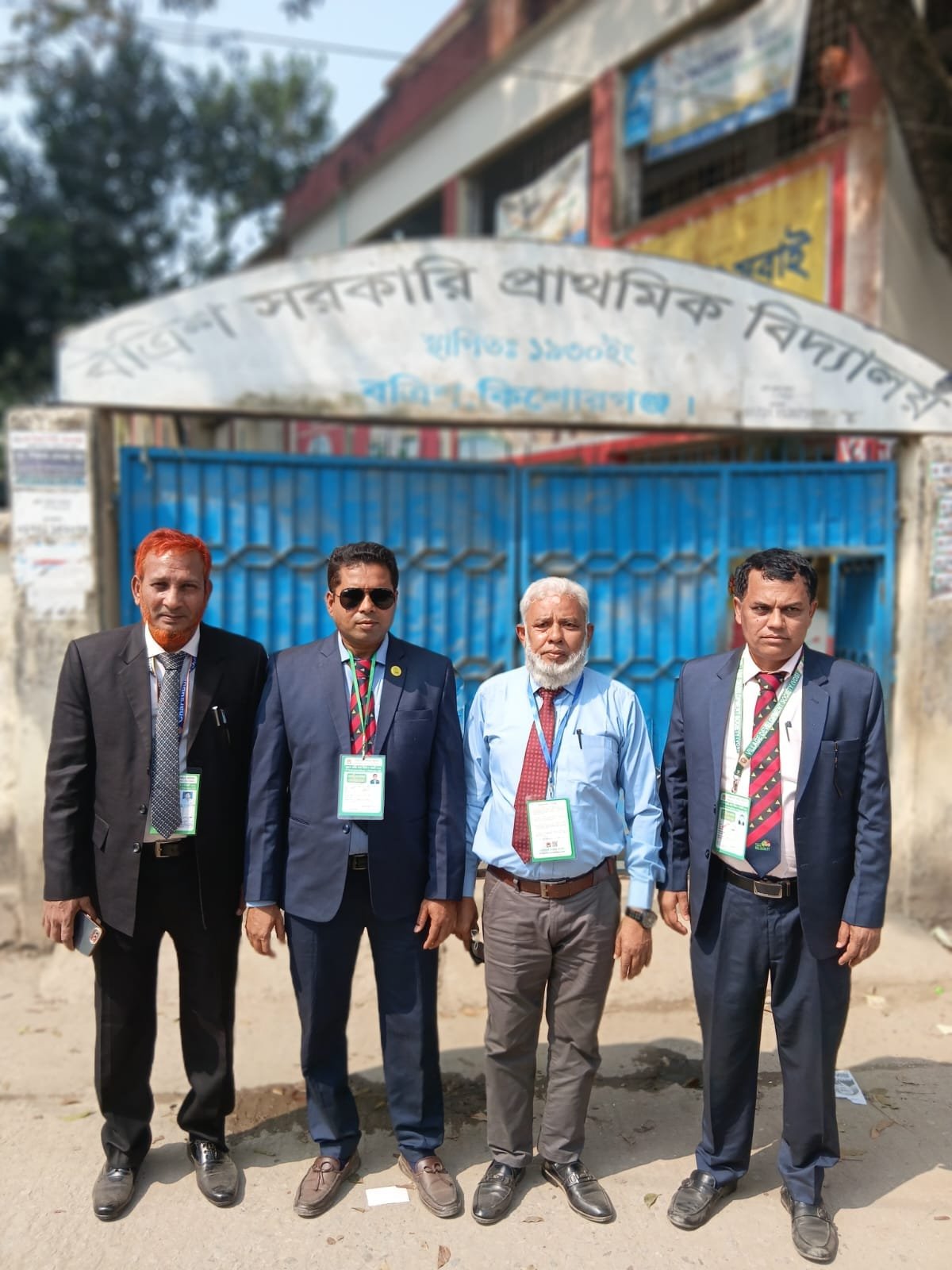 Four officials standing in front of a school gate